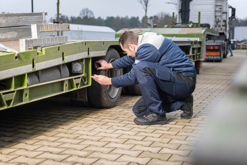 Monteur inspecteert vrachtwagenonderdeel op terrein.