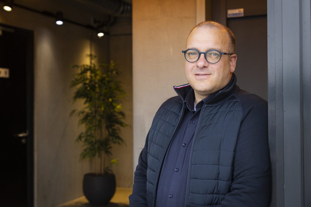 Man in jas leunt tegen muur.