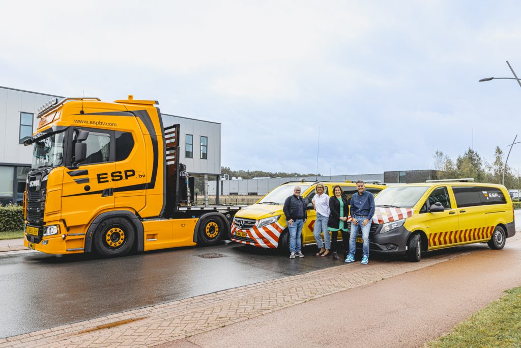 Gele vrachtwagen en busjes met mensen op industrieterrein